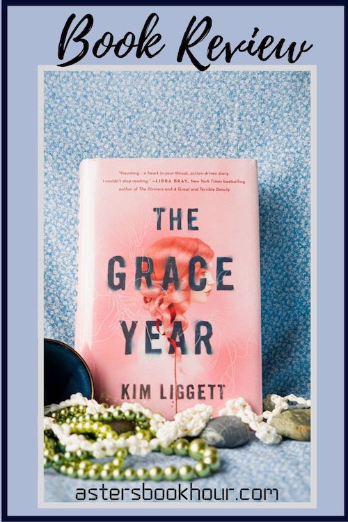The pinterest image for The Grace Year by Kim Liggett book review. There is a blue floral print background with the novel centered in the middle and the cover facing the front.