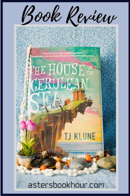 The pinterest image for The House in the Cerulean Sea by TJ Klune book review. There is a blue floral print background with the novel centered in the middle and the cover facing the front.
