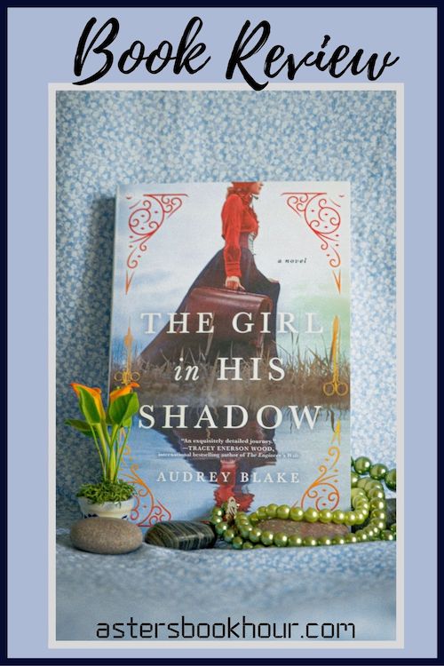 The pinterest image for The Girl in His Shadow by Audrey Blake book review. There is a blue floral print background with the novel centered in the middle and the cover facing the front.