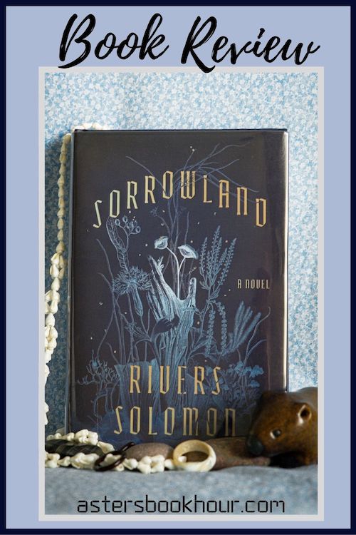 The pinterest image for Sorrowland by Rivers Solomon book review. There is a blue floral print background with the novel centered in the middle and the cover facing the front.