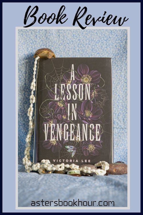 The pinterest image for A Lesson in Vengeance by Victoria Lee book review. There is a blue floral print background with the novel centered in the middle and the cover facing the front.