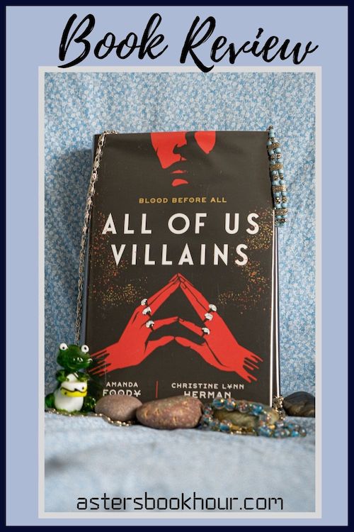 The pinterest image for All of Us Villains book review. There is a blue floral print background with the novel centered in the middle and the cover facing the front.
